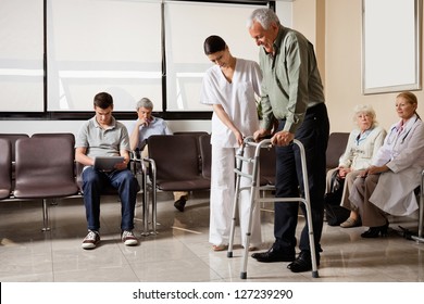 Senior man being helped by female nurse to walk the Zimmer frame with people sitting in hospital lobby - Powered by Shutterstock