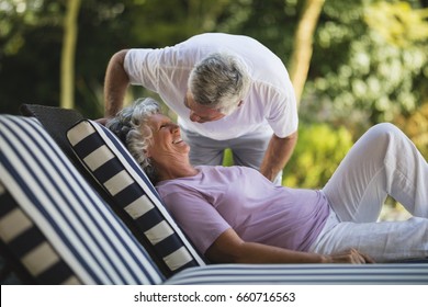 Senior Man Bending Over Smiling Woman Resting On Lounge Chair