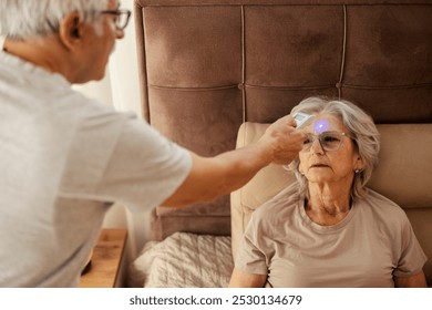 Senior man in blurry foreground measuring temperature with digital thermometer while his sick wife sitting in bed. - Powered by Shutterstock