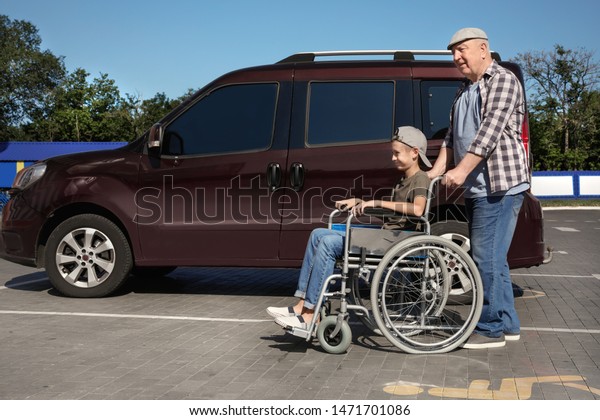 Senior\
man with boy in wheelchair near van on car\
parking