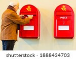 Senior man in brown leather jacket posting a letter in a Danish mailbox