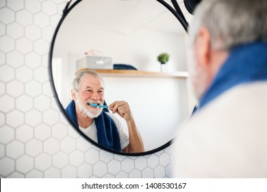 A senior man brushing teeth in bathroom indoors at home. Copy space.