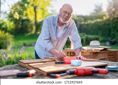 A Senior Man Is Building Wooden Planters For Permaculture Vegetable Garden On The Terrace