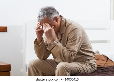 Senior man can not sleep. He is sitting on his bed with headache. - Powered by Shutterstock