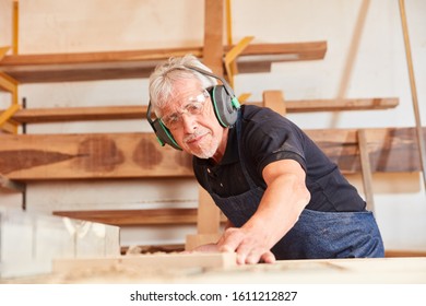 Senior man as carpenter saws wood in carpentry or joinery workshop - Powered by Shutterstock