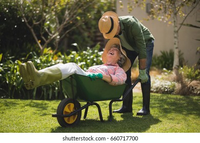 Senior Man Carrying Smiling Woman In Wheel Borrow At Yard