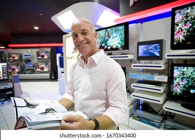 Senior Man With Catalogue In Electrical Store At Camera