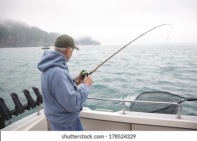 A Senior Man Catches A Salmon While Fishing In Alaska