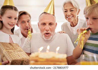 Senior man celebrating his birthday with his family at home, wearing party hats and blowing whistles. Grandpa blowing out birthday candles and making a wish surrounded by his grandkids, wife and son - Powered by Shutterstock