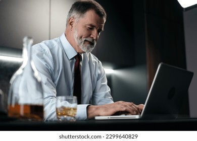Senior man checking using laptop in kitchen at home after work.