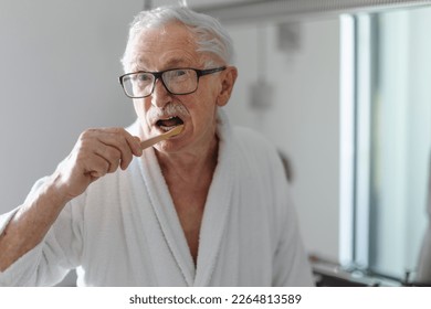 Senior man cleaning his teeth with wooden brush in bathroom, sustainable lifestyle. - Powered by Shutterstock