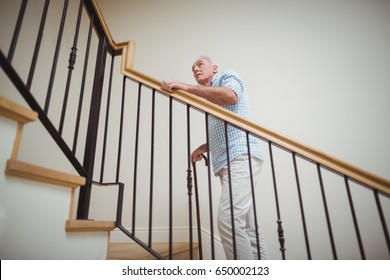 Senior Man Climbing Upstairs With Walking Stick At Home