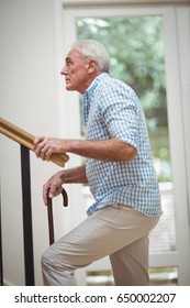 Senior Man Climbing Upstairs With Walking Stick At Home