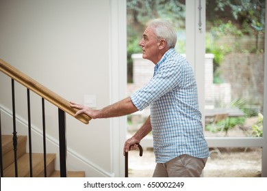 Senior man climbing upstairs with walking stick at home - Powered by Shutterstock