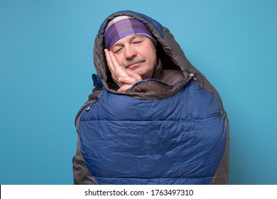 Senior Man In Comfortable Sleeping Bag On Blue Wall. Studio Shot