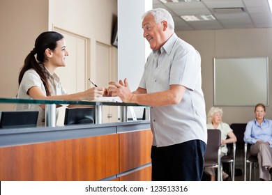 Senior man communicating with female receptionist while women sitting in background