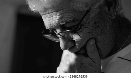 Senior man considering options in monochrome black and white. Dramatic elderly person ponders problems with hand in chin