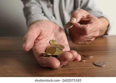 Senior man counting coins at wooden table, closeup. Financial problems