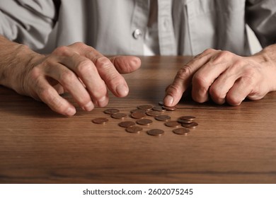 Senior man counting coins at wooden table, closeup. Financial problems