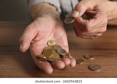 Senior man counting coins at wooden table, closeup. Financial problems