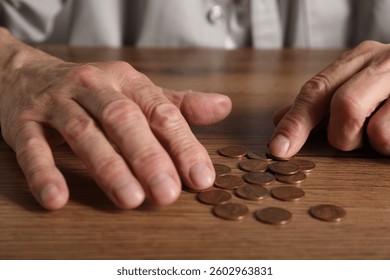 Senior man counting coins at wooden table, closeup. Financial problems