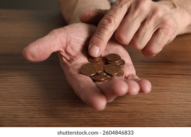 Senior man counting coins at wooden table, closeup. Financial problems