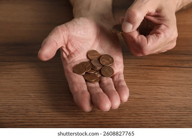 Senior man counting coins at wooden table, closeup. Financial problems