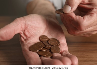 Senior man counting coins at wooden table, closeup. Financial problems