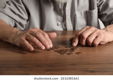 Senior man counting coins at wooden table, closeup. Financial problems