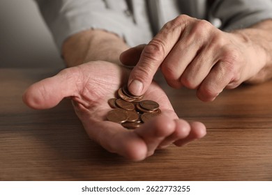 Senior man counting coins at wooden table, closeup. Financial problems