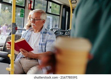 A Senior Man Is In A Crowded Bus And Reading A Book To His Destination