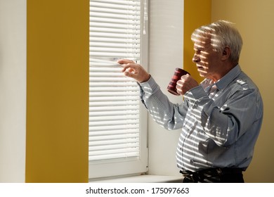 Senior man with cup looking out the window through jalousie  - Powered by Shutterstock