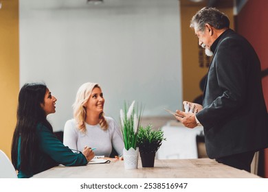 Senior man director standing by the conference desk, talking to two women employees, one young Indian woman his secretary and another caucasian disabled woman on a wheelchair. Three diverse multi ethn - Powered by Shutterstock