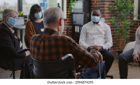Senior Man With Disability Attending Aa Group Therapy Session With People During Pandemic. Person With Face Mask Sitting In Wheelchair And Talking About Alcohol Addiction At Meeting.