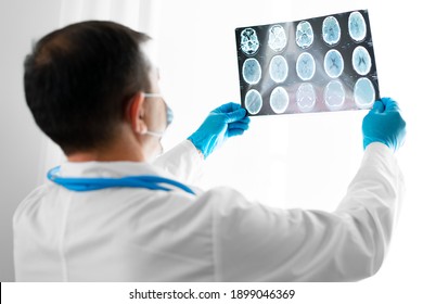 Senior Man Doctor In Mask Examines Head MRI In Hospital