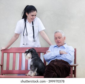 Senior Man With Dog Sitting On The Bench While Young Smiling Nurse Standing Behind Him 