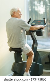 Senior Man Doing Exercise On A Bike In A Fitness Club