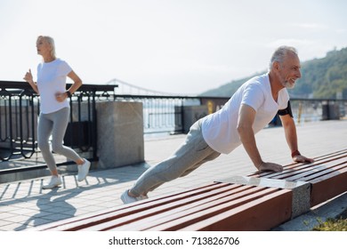 Senior man doing push-ups while his wife jogging