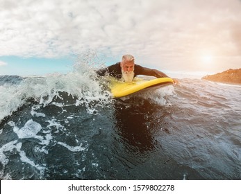 Senior man doing surf with longboard riding a wave - Happy old guy having fun doing extreme sport - Joyful elderly concept - Focus on his face - Powered by Shutterstock