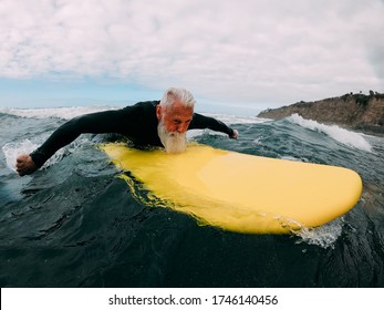 Senior man doing surf with longboard riding a wave - Mature person having fun doing extreme sport - Joyful elderly concept - Focus on his face - Powered by Shutterstock