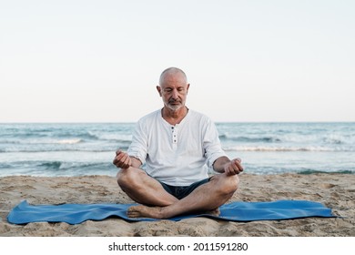 Senior Man Doing Yoga Meditation Outdoor At The Beach - Elderly And Healthy Lifestyle - Focus On Face