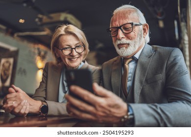 senior man dressed in a suit and a mature blonde woman as business partners husband and wife friends or father daughter talk With smartphones in hand browse internet exchange ideas copy space - Powered by Shutterstock