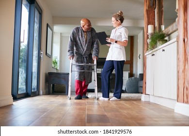 Senior Man In Dressing Gown Using Walking Frame Being Helped By Female Nurse With Clipboard