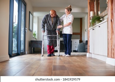 Senior Man In Dressing Gown Using Walking Frame Being Helped By Female Care Worker