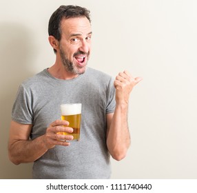 Senior man drinking beer pointing with hand and finger up with happy face smiling