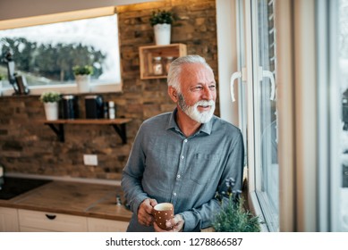 Senior Man Drinking Coffee In The Kitchen, Looking At Window On Winter Day.