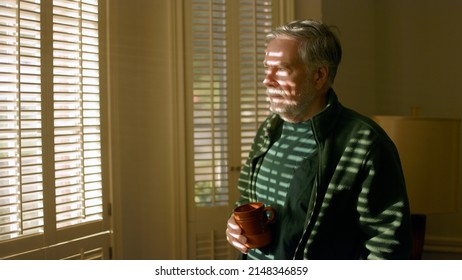 Senior man drinking coffee in the morning next to a brightly lit window