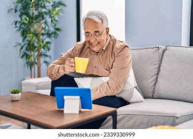 Senior man drinking coffee watching touchpad at home - Powered by Shutterstock