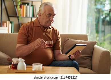 Senior Man Drinking Tea And Watching News On Tablet Computer In The Morning