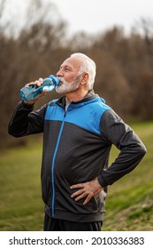 Senior man is drinking water after exercising in park.
